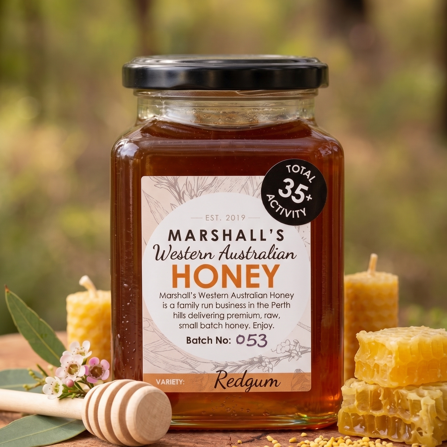 Jar of Marshall's Western Australian Honey on a wooden surface with honeycomb and flowers in the background.