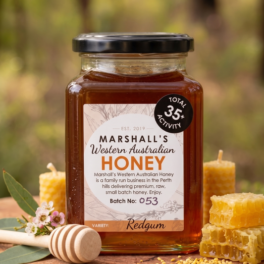 Jar of Marshall's Western Australian Honey on a wooden surface with honeycomb and flowers in the background.