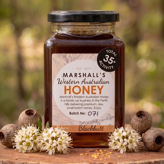 Jar of Marshall's Western Australian Honey on a wooden surface with flowers and honeycomb pieces.
